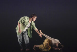 Michael in a green shirt putting his arm out to Madelene who is curled up on the floor.