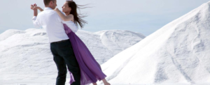 Michelle Ryan in a purple dress dancing with a man in black pants and a white shirt on hills of white salt.