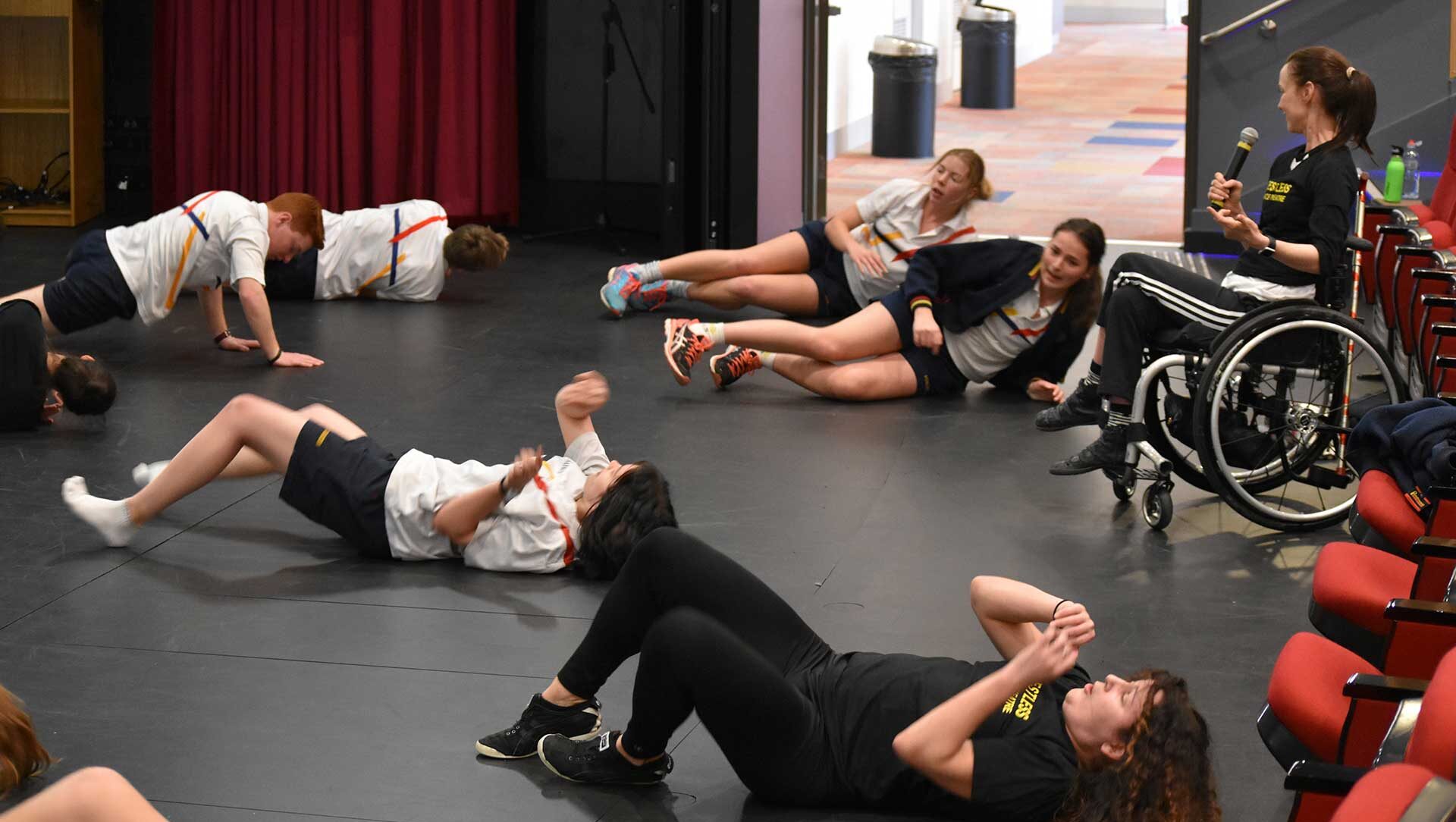 a group of students lying on the floor of the studio as Michelle holds a microphone, leading the workshop