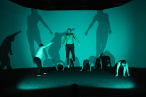 Dancer jumping with 5 other dancers behind him all in green light.